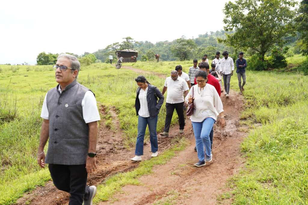 A group walks along a dirt path through green fields with hills in the background