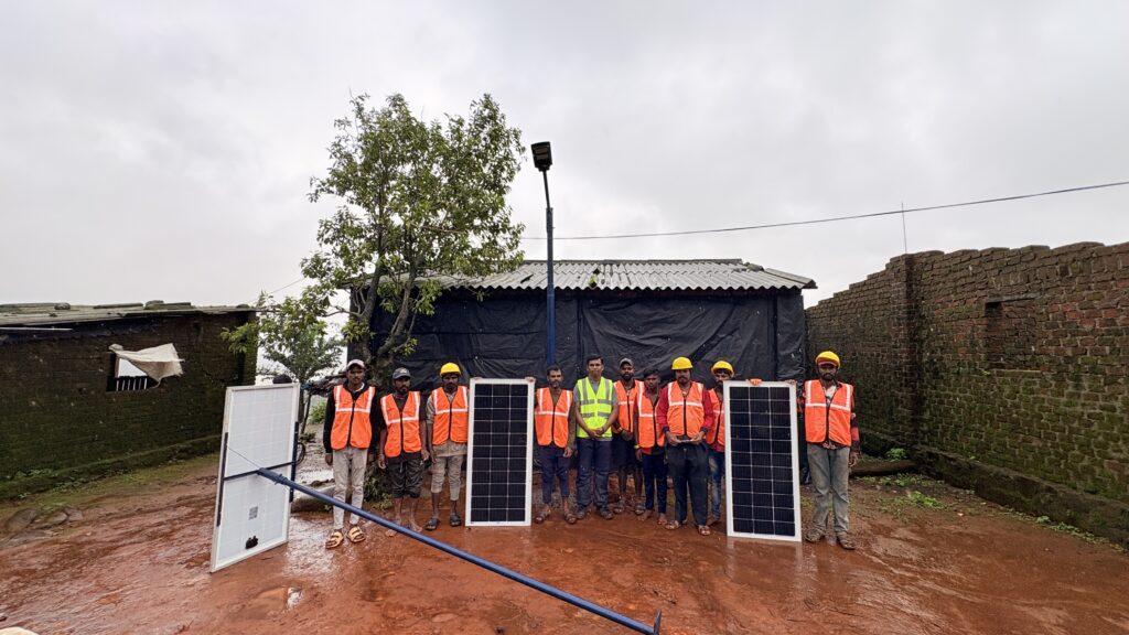 Field team in orange safety vests and hard hats standing with solar panels and electrical equipment in wet ground under overcast sky
