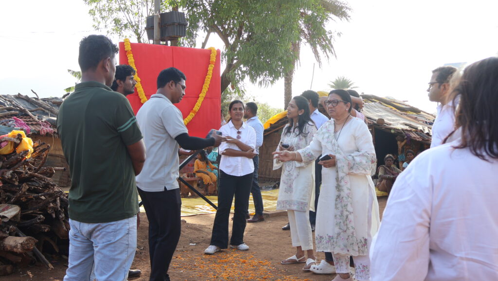 Group gathered outdoors in front of decorated red backdrop with marigold garlands during daytime ceremony