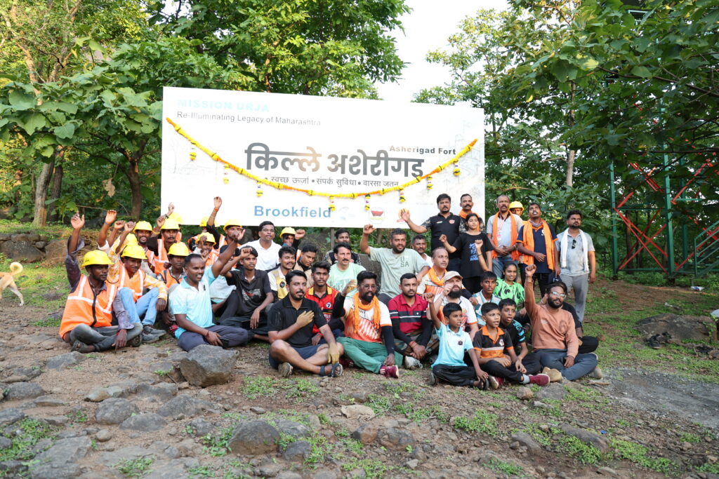 Group of volunteers in safety vests and hard hats seated and standing outdoors with banner reading Kille Asherigad and Brookfield