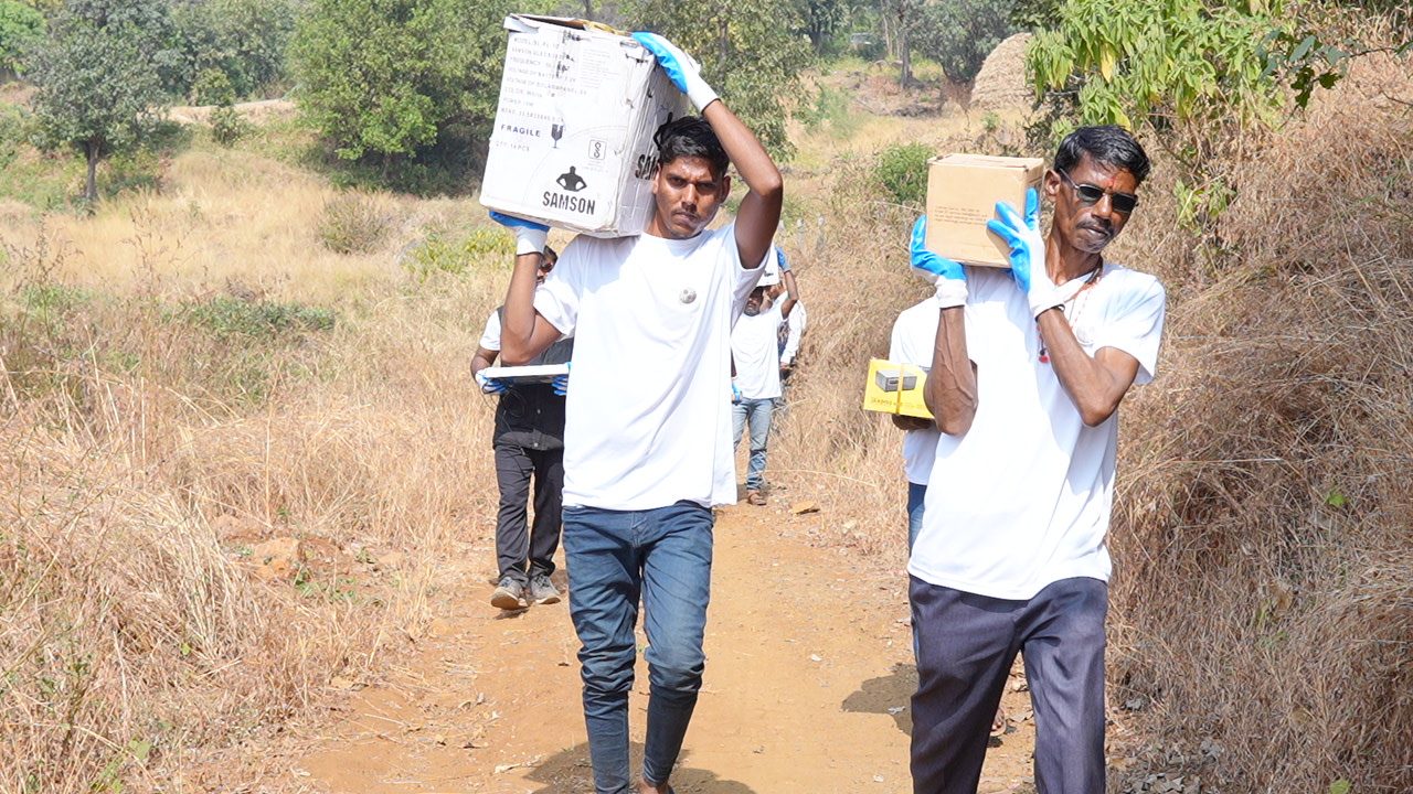 Carrying solar kits up to a hamlet. At volume, logistics is the real work.